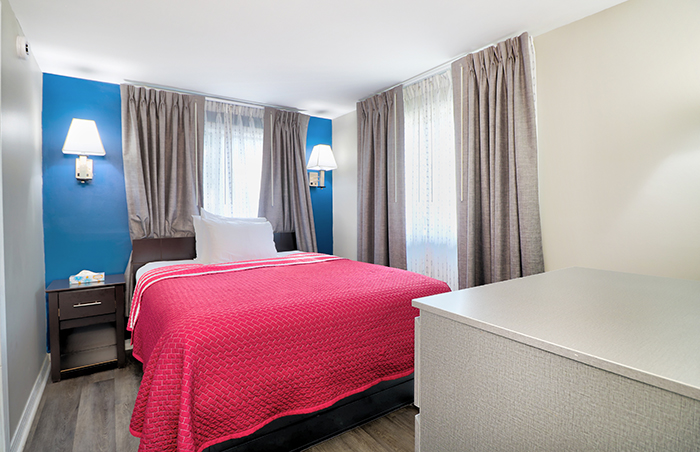 A hotel room with a red bedspread, white pillows, and a nightstand with a lamp.