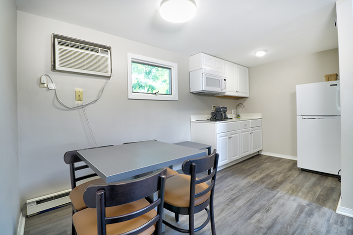 A small kitchenette with a table, chairs, refrigerator, microwave, and air conditioner.