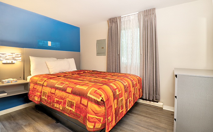 A hotel room with a bed, dresser, and window