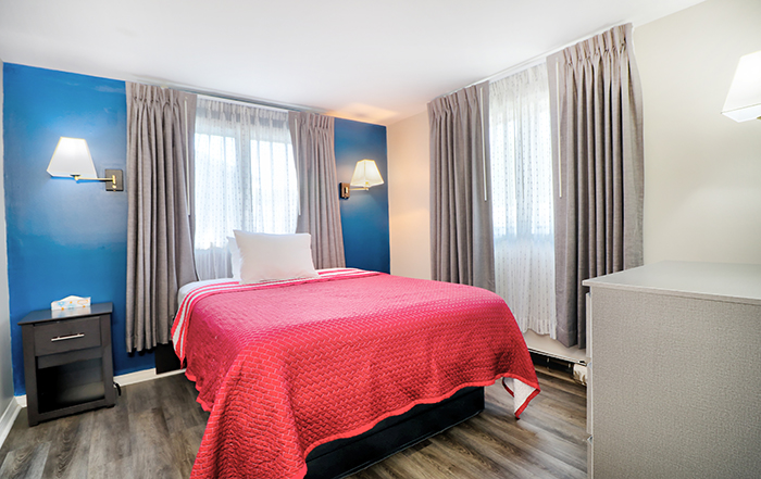 A hotel room with a red bedspread, a nightstand, and a window with curtains.