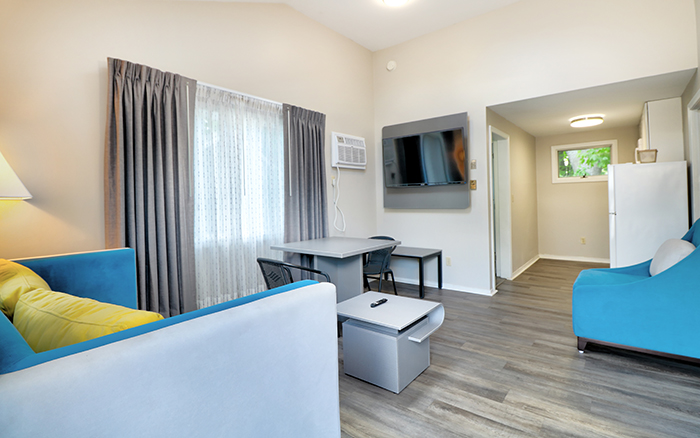 A wide view of a hotel room with a sofa, TV, table, and refrigerator.